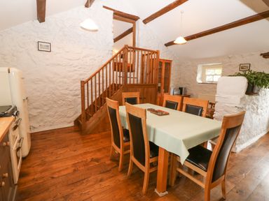 A dining area with wooden table and chairs next to staircase and white stone walls at Nant Bach Boduan near Nefyn