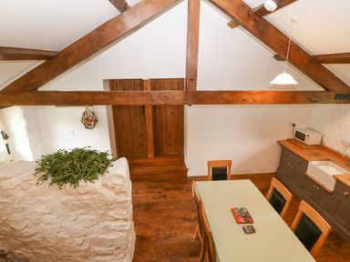 A dining area with a table and chairs wooden beams and a kitchen counter with a microwave at Nant Bach Boduan near Nefyn