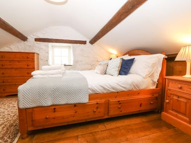 A bedroom with a wooden bed with pillows and folded towels a wooden dresser and bedside table with a lamp at Nant Bach Boduan near Nefyn