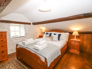 A bedroom with a wooden bed with folded towels and pillows a nightstand with a lamp and a chest of drawers Nant Bach Boduan near Nefyn