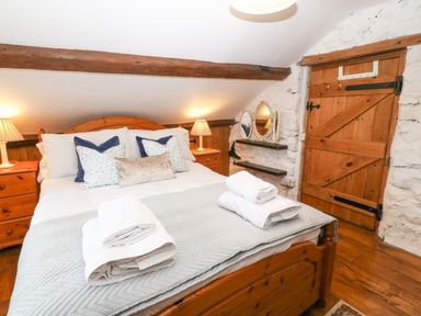 A bedroom with a wooden bed with pillows and towels wooden door stone wall and bedside tables with lamps at Nant Bach Boduan near Nefyn