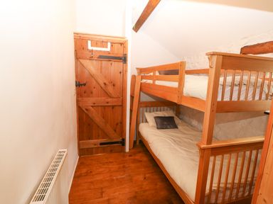 A small bedroom with wooden bunk beds and a wooden door with black hinges at Nant Bach Boduan near Nefyn