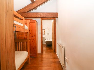 A hallway with wooden bunk beds a wooden wardrobe and a radiator leading to a bathroom with a bathtub at Nant Bach Boduan near Nefyn