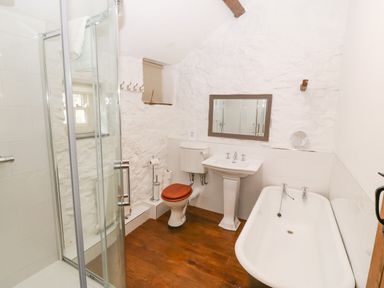 A bathroom with a glass shower enclosure toilet with wooden seat pedestal sink and bathtub at Nant Bach Boduan near Nefyn