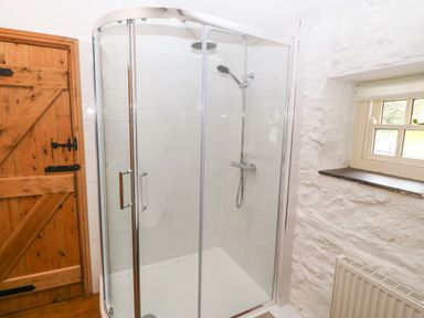 A bathroom with a glass shower enclosure next to a wooden door and a small window at Nant Bach in Boduan near Nefyn