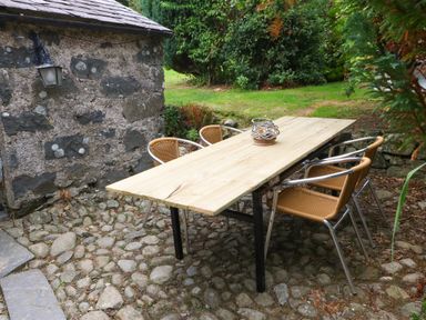 An outdoor stone patio with a wooden table and four chairs next to a stone wall with a lamp Nant Bach Boduan near Nefyn