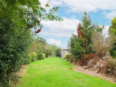 A grass lawn with bushes and trees on both sides near a stone building at Nant Bach in Boduan near Nefyn