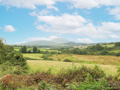 An open rural landscape with fields bushes and distant hills under a blue sky at Nant Bach in Boduan near Nefyn