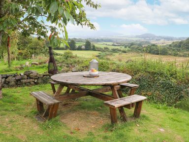 A wooden round picnic table with benches on grass overlooking countryside at Nant Bach in Boduan near Nefyn