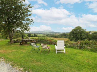 An outdoor area with three chairs and a picnic table under a tree overlooking fields and hills at Nant Bach in Boduan near Nefyn
