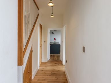 A hallway with wooden flooring and doors leading to a kitchen with a countertop and flowers at Wottonsbury in Ilsington