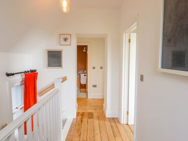 A hallway with wooden floor white walls and a window with orange curtains at Wottonsbury in Ilsington