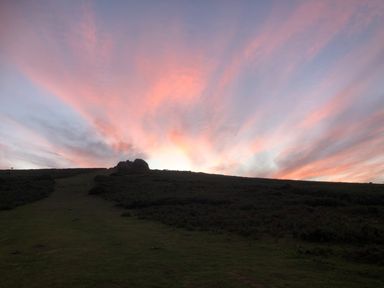 A hillside with rocks and vegetation under a sky with pink and purple clouds at Wottonsbury in Ilsington
