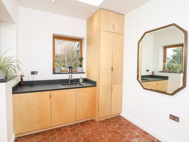 A kitchen area with wooden cabinets a black countertop a window with plants and an octagonal mirror on the wall at Wottonsbury in Ilsington