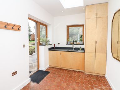 A kitchen area with wooden cabinets a sink and potted plants on the windowsill at Wottonsbury in Ilsington
