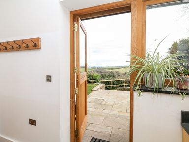 A doorway opening to a stone patio with a plant on the window sill at Wottonsbury in Ilsington
