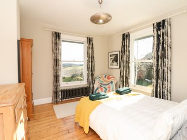 A bedroom with a bed, wooden dresser, armchair, two windows with curtains and a radiator at Wottonsbury in Ilsington