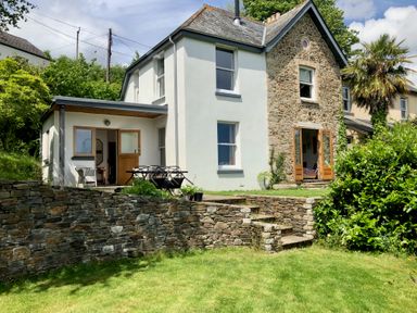 A two-story house with stone and white walls with a lawn and stone wall in front at Wottonsbury in Ilsington