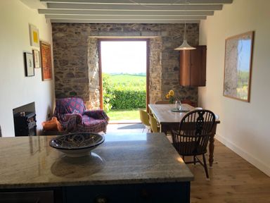 A dining area with a wooden table and chairs beside a stone wall opening to a garden at Wottonsbury in Ilsington