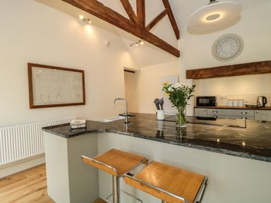 A kitchen with a black countertop island and wooden stools at Tom's Barn in Mudford Sock near Yeovil Somerset