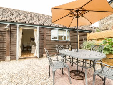 A patio with a metal table and chairs under an umbrella outside a wooden building at Toms Barn Mudford Sock near Yeovil Somerset