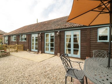 An outdoor patio with a metal table and chairs under a large umbrella beside a wooden building with blue window and door frames at Tom's Barn Mudford Sock near Yeovil Somerset