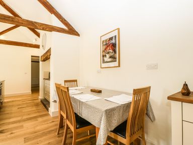A dining area with a wooden table and four chairs a framed coffee poster on the wall and exposed wooden beams on the ceiling at Toms Barn in Mudford Sock near Yeovil Somerset
