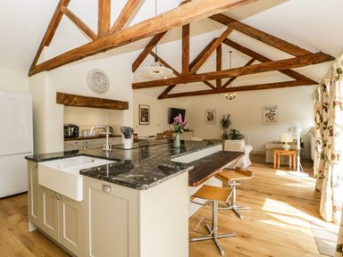 A kitchen and living area with a marble countertop island bar stools exposed wooden beams and wooden floor at Toms Barn in Mudford Sock near Yeovil Somerset