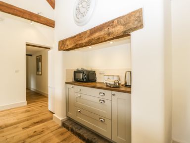 A kitchen area with wooden countertop cabinets a microwave kettle and a basket under a wooden beam at Toms Barn in Mudford Sock near Yeovil Somerset