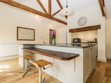 A kitchen with a wooden breakfast bar two stools and exposed wooden beams at Tom's Barn Mudford Sock near Yeovil Somerset