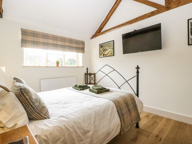 A bedroom with a double bed two folded towels on the bed a wall-mounted television and wooden beams at Tom's Barn in Mudford Sock near Yeovil Somerset