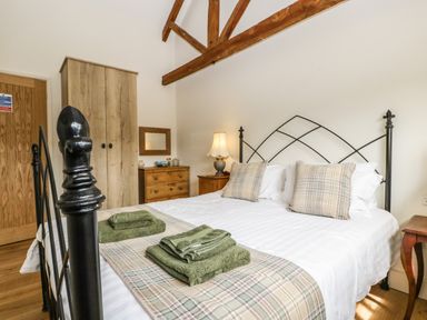 A bedroom with a metal bed frame pillows and folded towels on the bed a wooden wardrobe and chest of drawers with a lamp at Tom's Barn in Mudford Sock near Yeovil Somerset