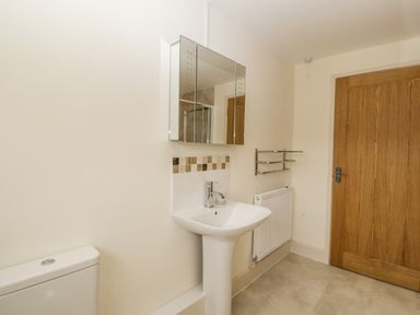 A bathroom with a pedestal sink mirror towel rack radiator and wooden door at Toms Barn in Mudford Sock near Yeovil Somerset