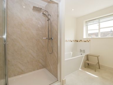A bathroom with a shower enclosure and a bathtub with a small step stool near a window at Toms Barn in Mudford Sock near Yeovil Somerset