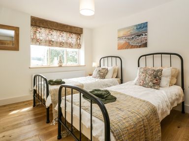 A bedroom with two single beds with floral pillows and blankets a window with floral curtains and a seascape painting on the wall at Toms Barn in Mudford Sock near Yeovil Somerset
