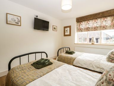 A bedroom with two single beds green towels on the beds a wall-mounted tv and a window with floral curtains at Tom's Barn Mudford Sock near Yeovil Somerset