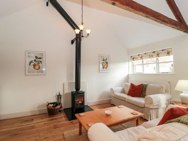 A living room with a wood stove and two sofas near a window at Toms Barn in Mudford Sock near Yeovil Somerset