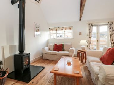 A living room with two sofas a wooden coffee table a black wood stove and windows with floral curtains at Toms Barn in Mudford Sock near Yeovil Somerset