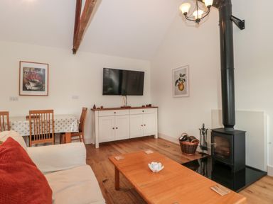 A living room with a wood stove a TV mounted above a sideboard and a wooden dining table at Toms Barn in Mudford Sock near Yeovil Somerset