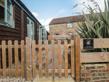 A wooden gate leading to a stone path between two buildings with blue windows at Tom's Barn in Mudford Sock near Yeovil Somerset
