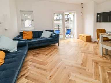 A living room with blue sofas and a small dining area near a balcony at Harbour Hideaway in Looe