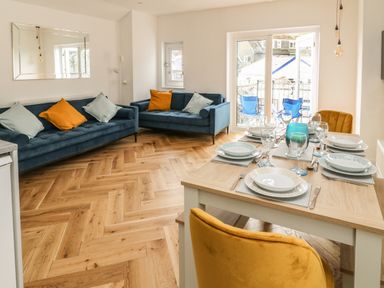 A dining area with a set table and a seating area with two blue sofas and orange and light blue cushions at Harbour Hideaway in Looe