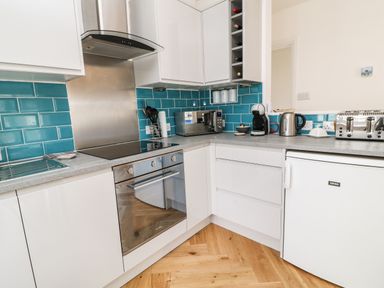 A kitchen with white cabinets blue tiled backsplash and appliances at Harbour Hideaway in Looe