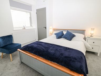 A bedroom with a bed and blue cushions a blue chair and a bedside table with a lamp at Harbour Hideaway in Looe