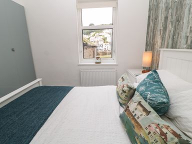 A bedroom with a bed pillows a lamp window and a wardrobe at Harbour Hideaway in Looe