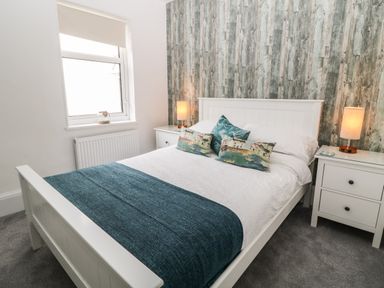 A bedroom with a white bed blue blanket and decorative pillows next to white bedside tables with lamps at Harbour Hideaway in Looe