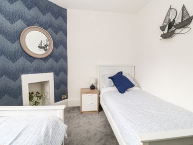 A bedroom with two single beds a nightstand with a lamp and wall decorations at Harbour Hideaway in Looe