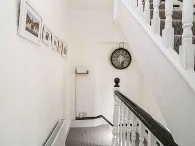 A staircase with a striped carpet a wall clock and framed pictures on the wall at Harbour Hideaway in Looe