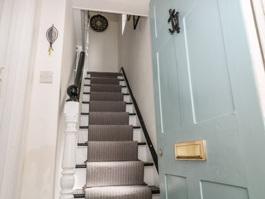 A staircase with a striped carpet runner and a light blue door with a brass mail slot at Harbour Hideaway in Looe