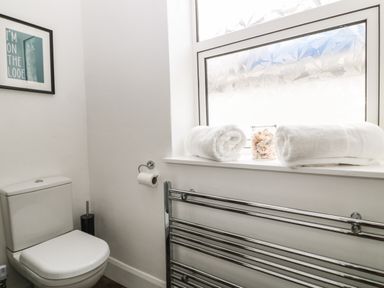 A bathroom with a toilet a towel rack two rolled towels and a framed picture at Harbour Hideaway in Looe